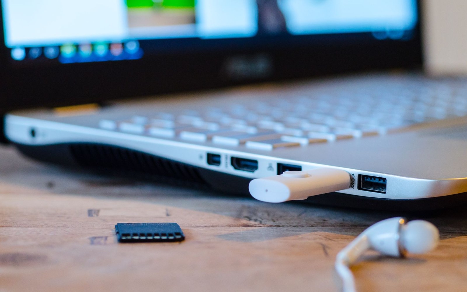 A USB flash drive plugged into a laptop's side port, with earbuds nearby on a wooden desk