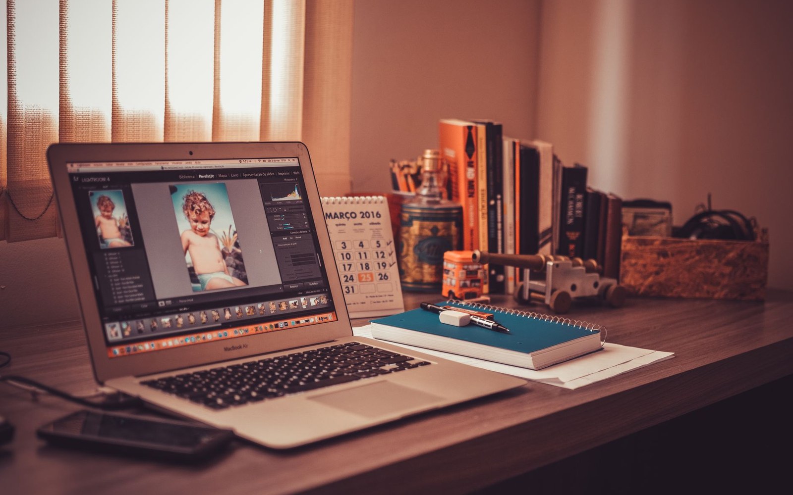 Laptop displaying photo editing software on a desk with a calendar and notebook