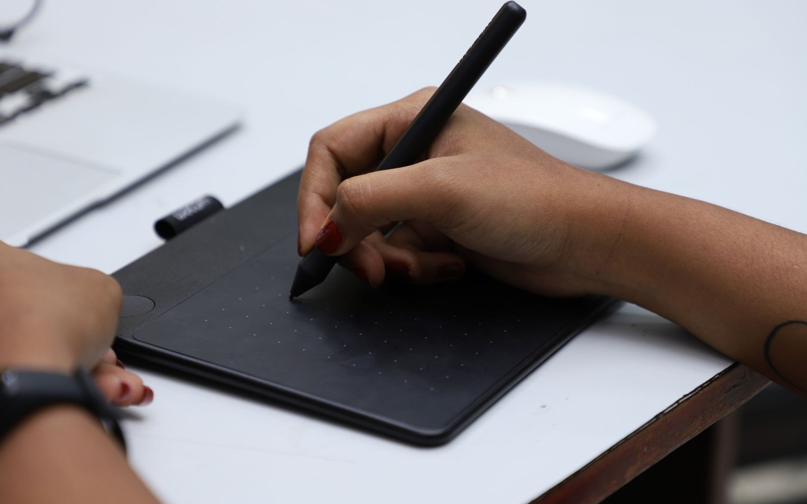 Wacom tablet and stylus with an adult illustrator's hand mid-stroke, monitor glow across the desk